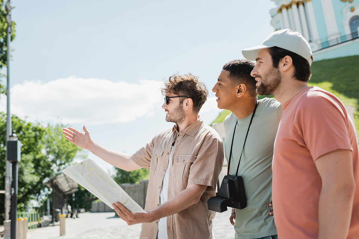 A tour guide is holding a map and pointing off into the distance as two tourists are looking onward.